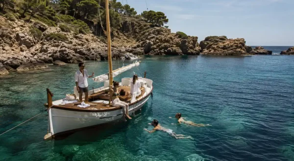Excursionistas contemplando una cala del Cap de Creus desde una barca tradicional en el Empordà.