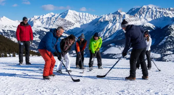 Participantes de una empresa jugando al hockey sobre nieve durante una jornada de team building en la montaña.